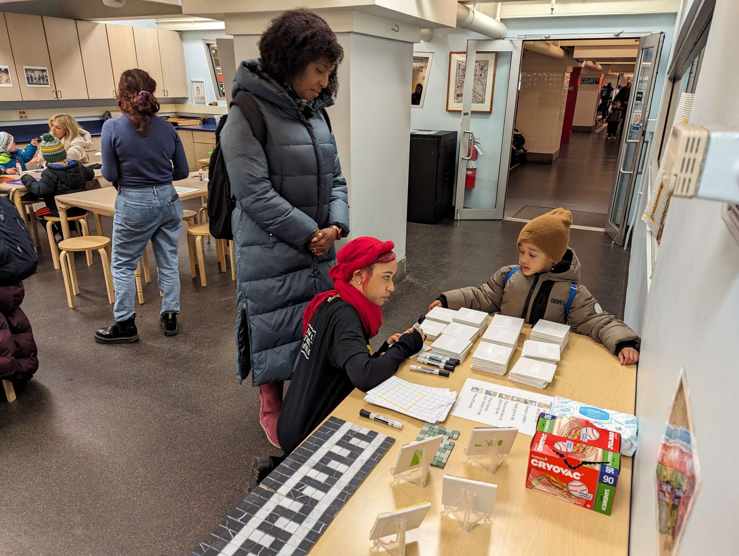 An adult and child talking to a Museum Educator next to a table filled with mosaic supplies.