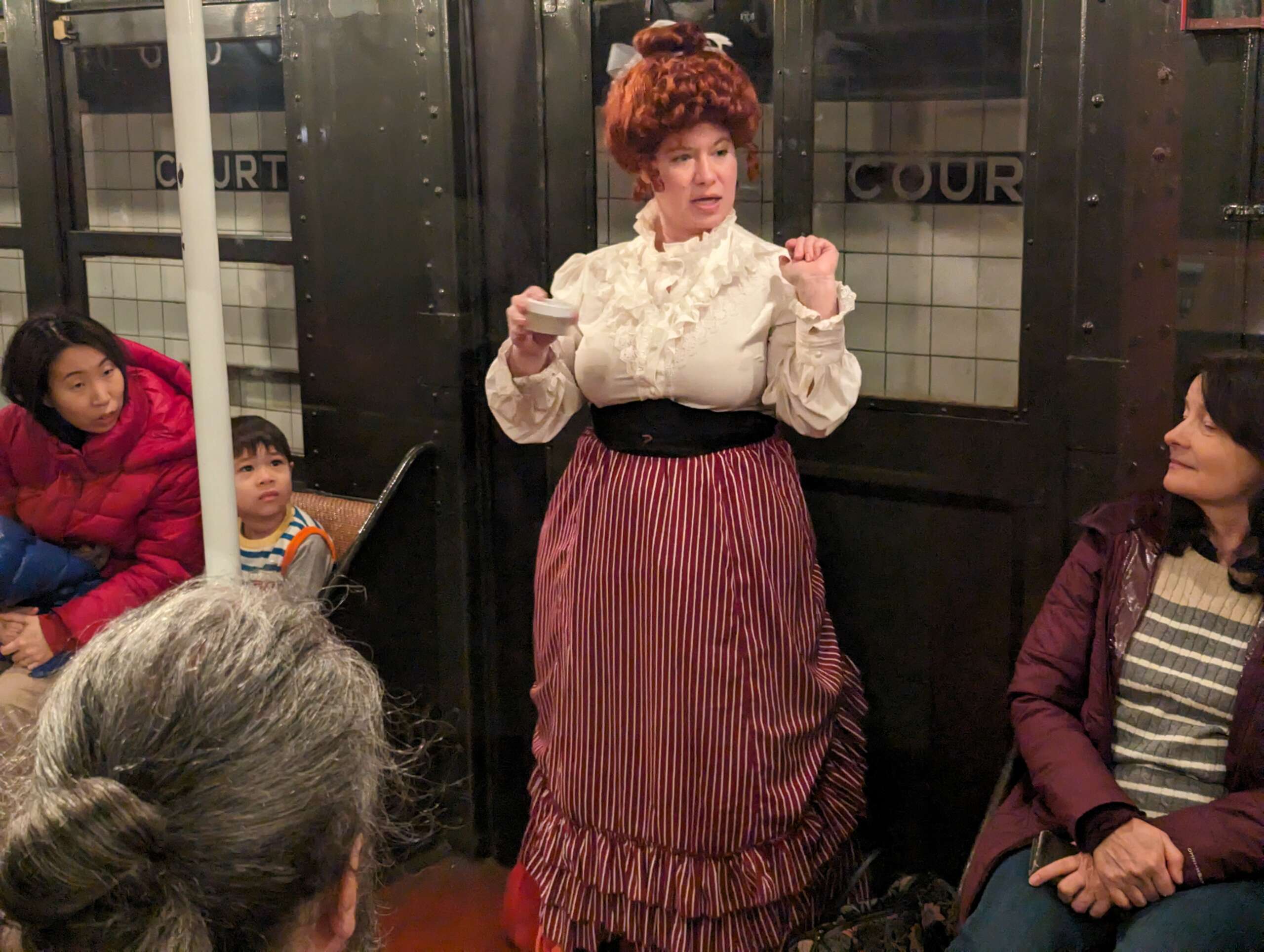 A Costumed Storyteller dressed as Mary Walton give a performance in a vintage train car attended by adults and children.