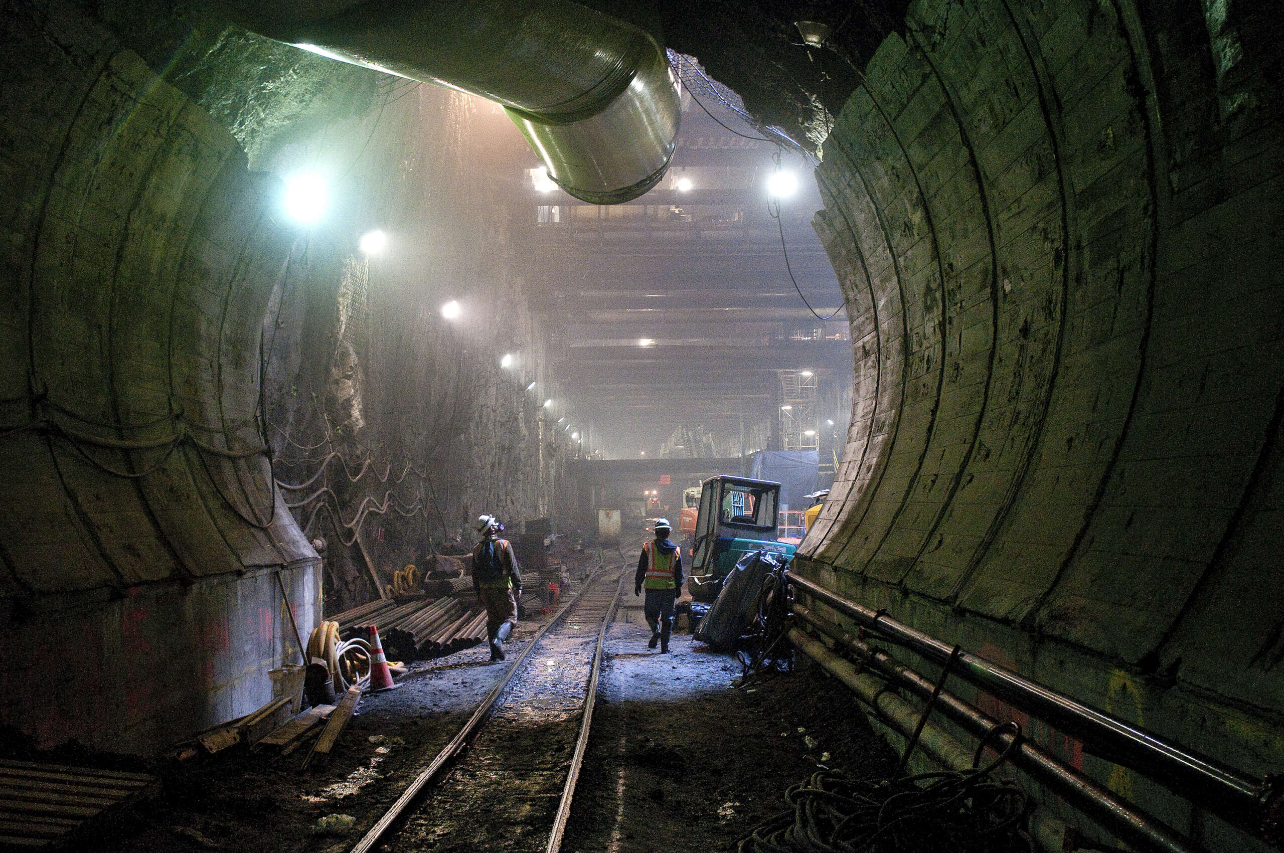 Image of tunnel under construction with tracks, open tubing and workers walking.