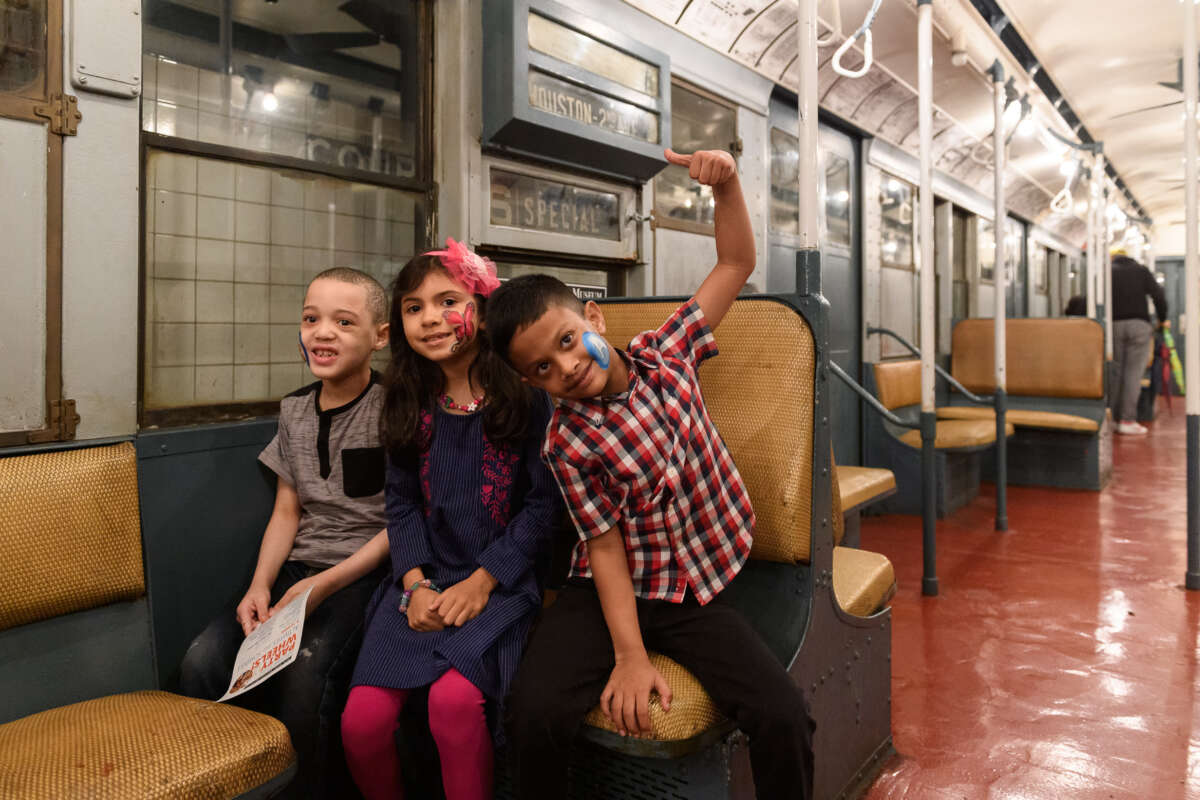 Three children with their face painted siting in a vintage subway car.