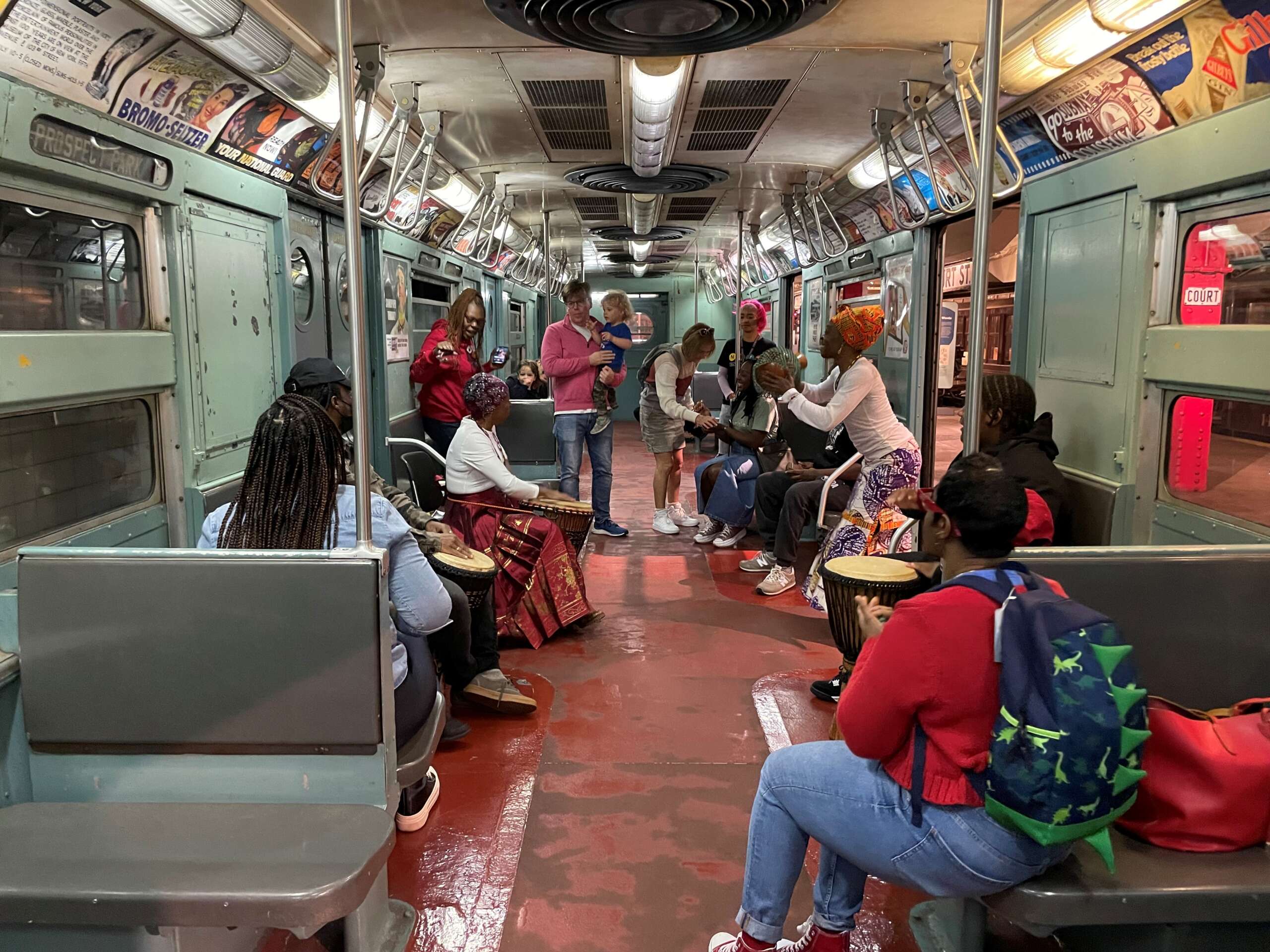 Families join in dancing and drumming on a vintage subway car.