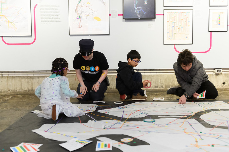 Kids and a NY Transit Museum staff sit on the R42 gallery floor making a large-scale map with art materials.