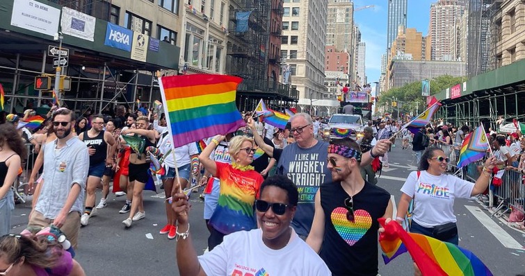 People walk down a street with rainbow flags for NYC Pride march.